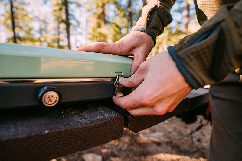 A man opens the latch on a green Eureka Ignite camp stove. 