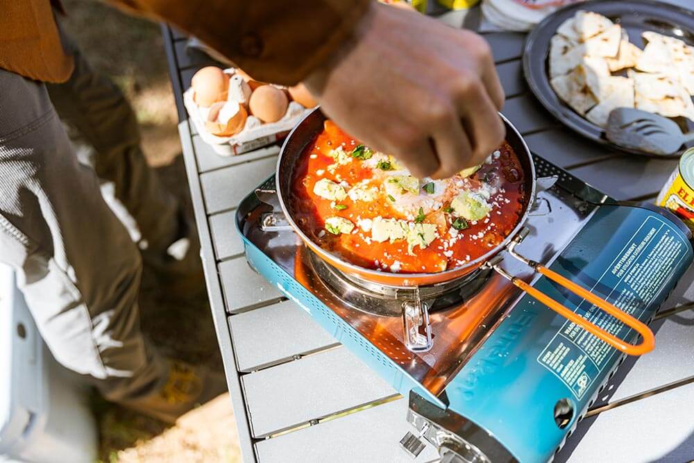 Sprinkling some seasoning into a delicious saucy dish cooked on the Eureka! SPRK Camp Stove