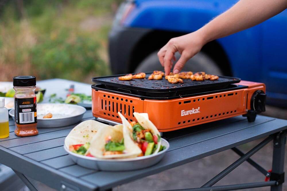 Sprinkling red chili flakes on a shrimp meal cooked on the Eureka! SPRK Camp Grill