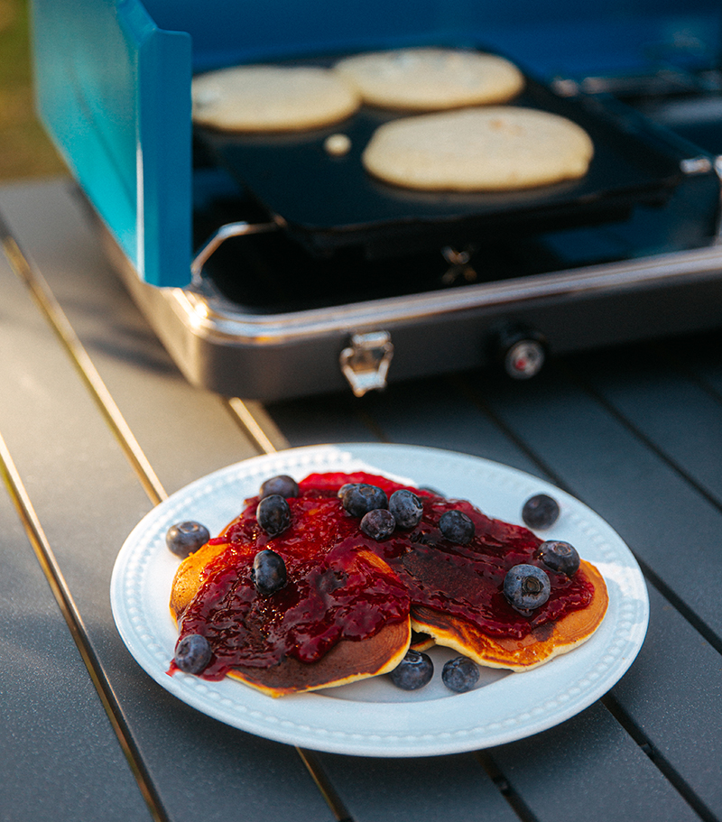 Pancakes with berries on a place in front of a camp stove.