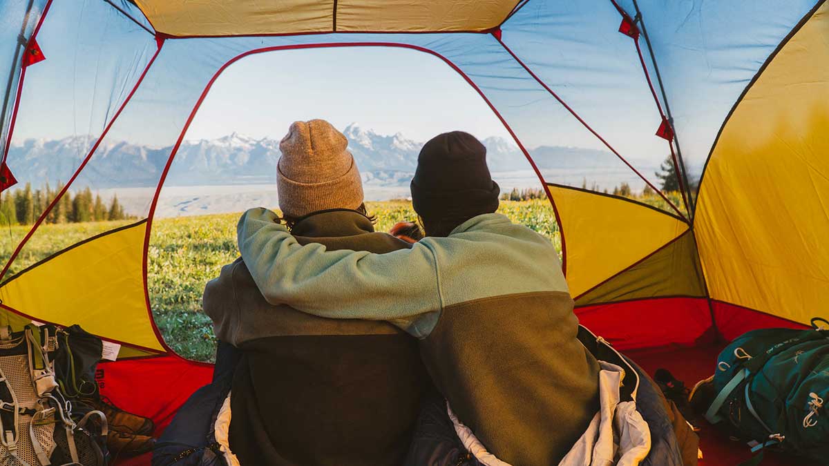 Two friends huddled up in a Eureka! tent looking outside into a beautiful horizon