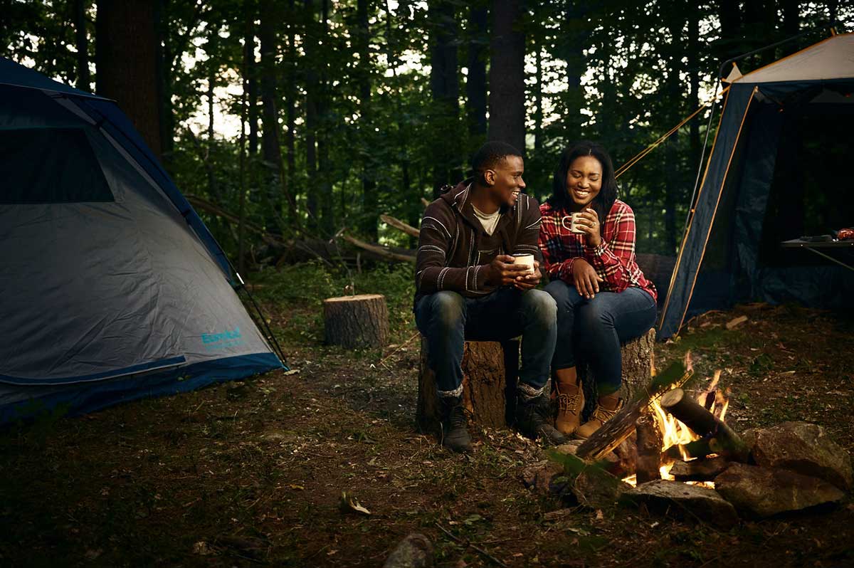 Couple cozying up together near campfire at campsite with hot beverages in hand