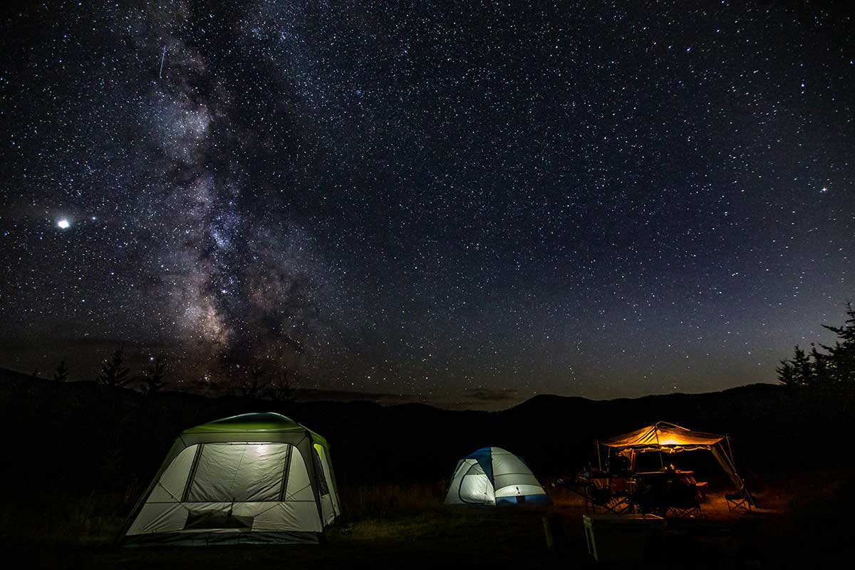 Beautiful shot of Eureka! tents at campfire with galaxy of stars in the night sky