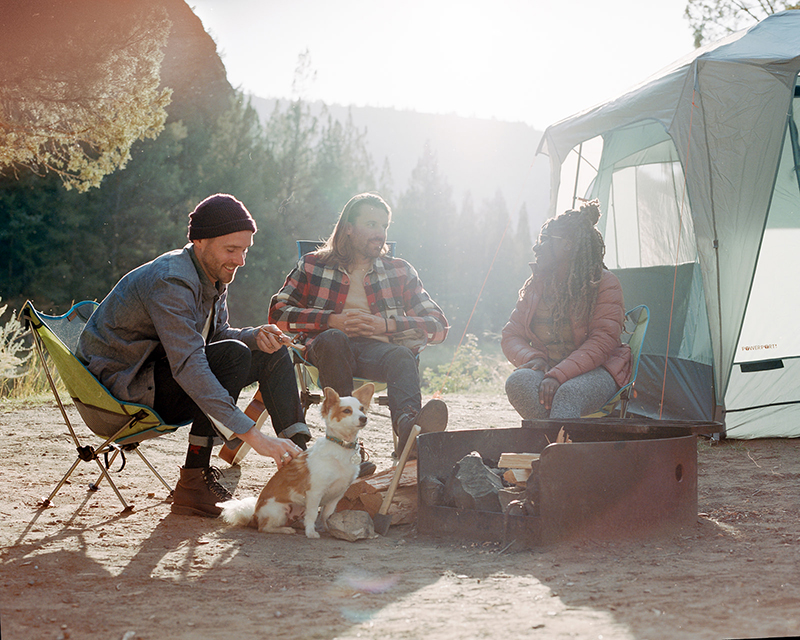 A small group of campers sits around a fire pit at their campsite. 