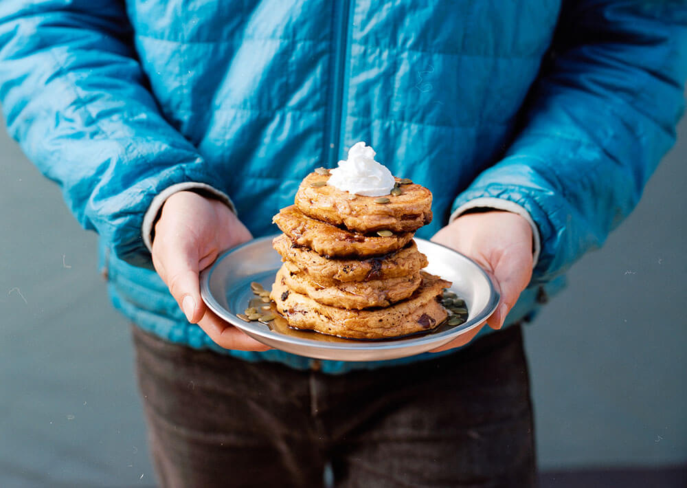 Holding a plate of stacked chocolate chip pumpkin pancakes topped with whipped cream