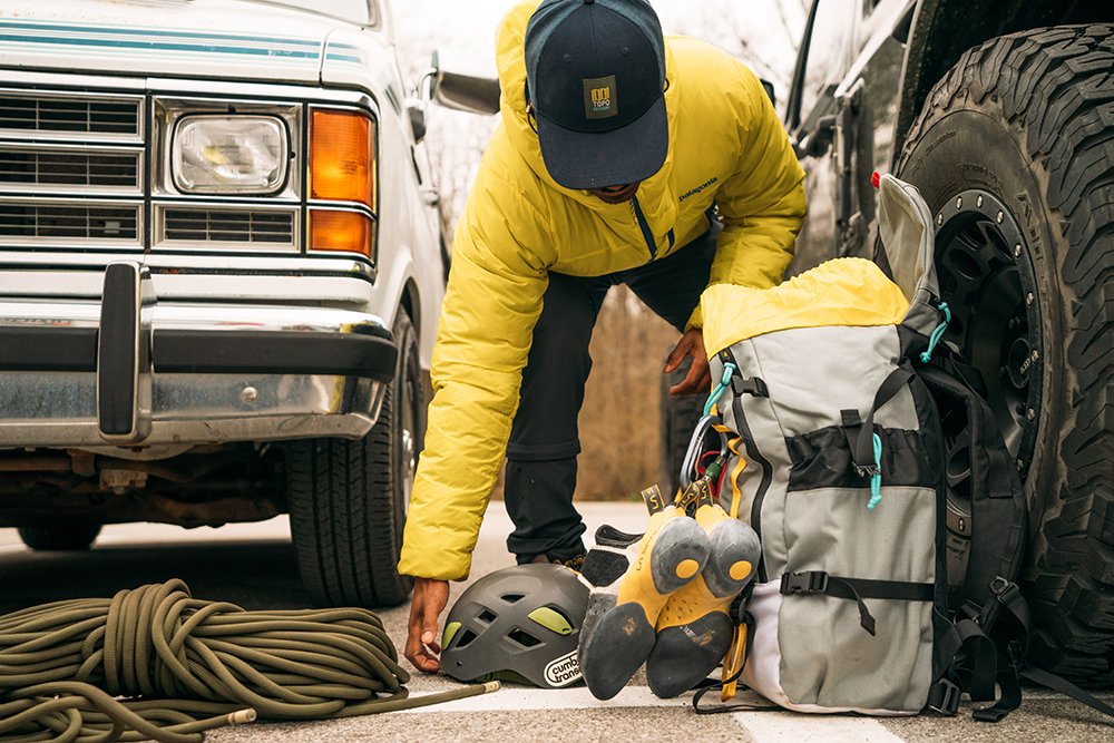 Caziah Franklin organizes climbing gear on the pavement in front of an old pickup truck.