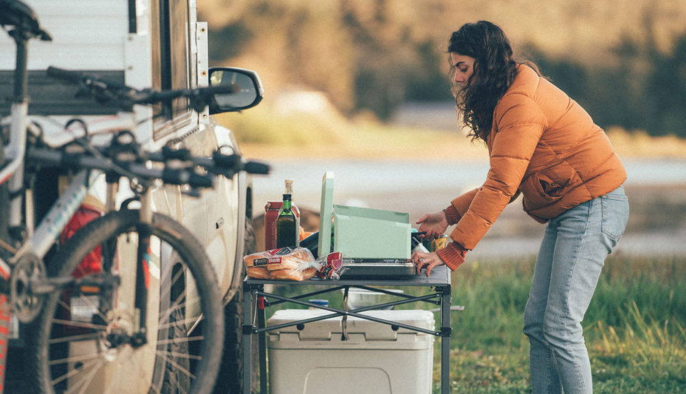 Kelsey Kagan cooks on a Eureka Ignite camp kitchen next to a camper truck. 