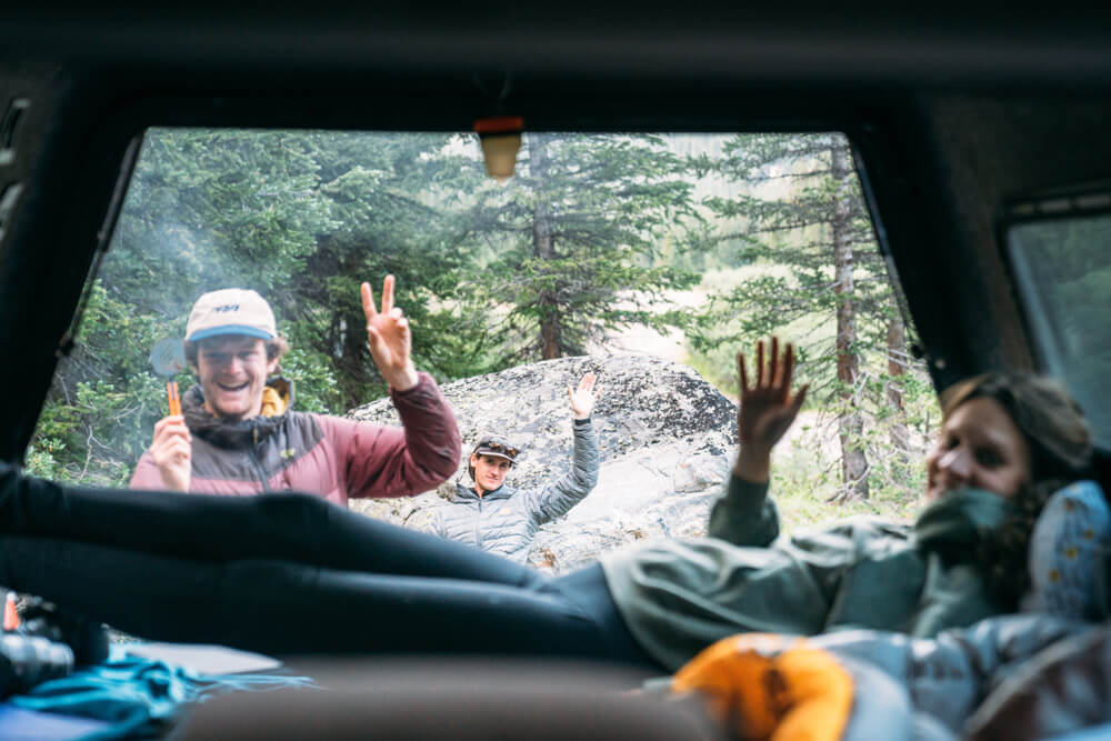 Group of friends waving to camera from view of inside camping vehicle