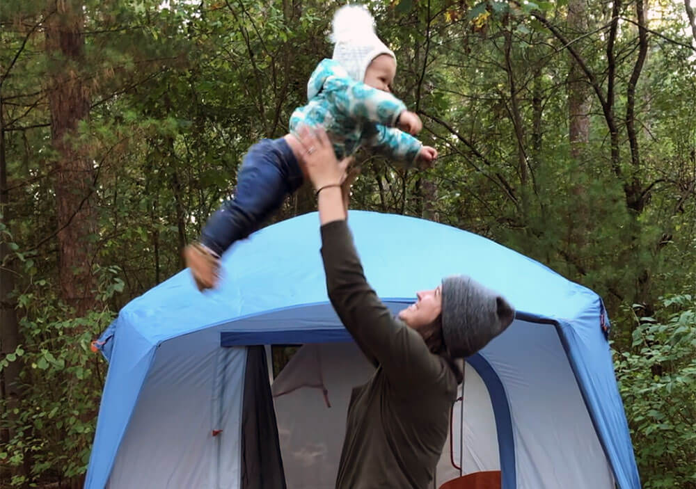 Woman tossing bundled up baby in the air at campsite