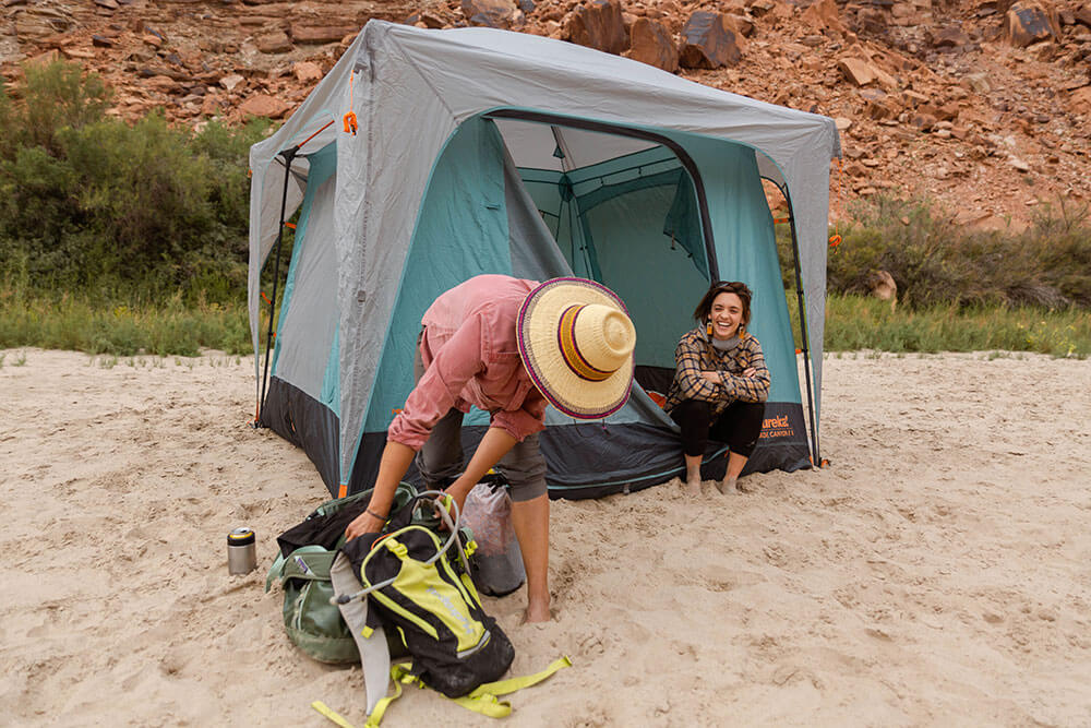 Woman rummaging through camp backpack while with giggling friend sitting in the Eureka! Jade Canyon tent