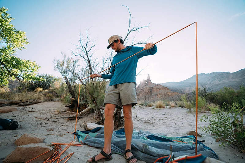 A young man assembles tent poles while pitching his tent at a campsite. 