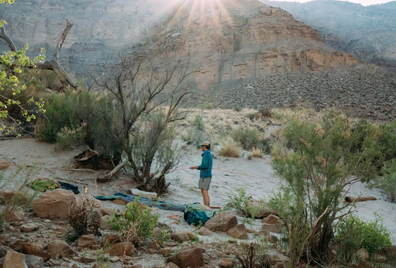 A young man pitches a tent and sets up his campsite in the desert. 