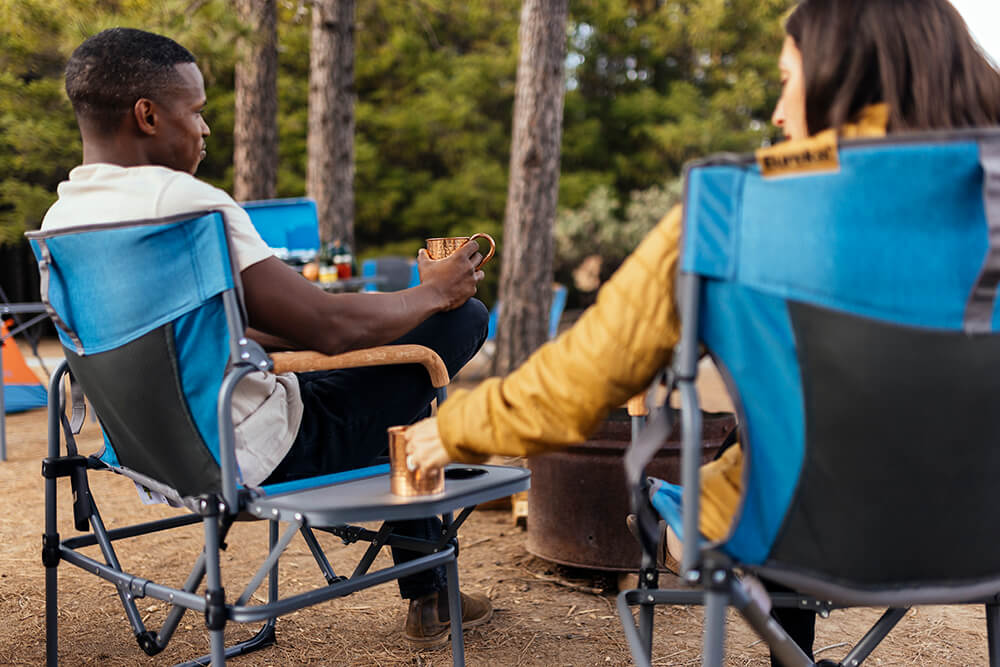 A man and woman sit in blue Eureka! camp chairs at a campsite. 