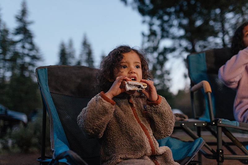 A young girl eats a s'more at a campfire. 