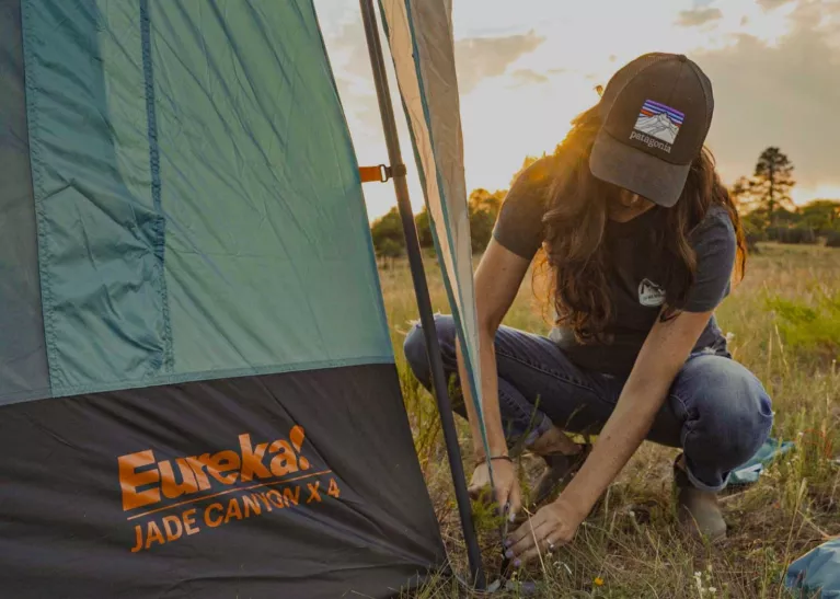 Woman placing stake in ground to secure Eureka Jade Canyon X 4 Car Camping Tent